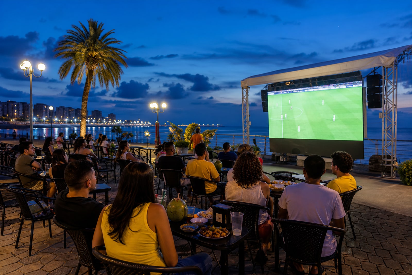 Publico acompanhando partida de futebol em tela ao ar livre na orla